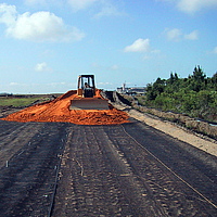 Un bulldozer sparge sabbia su una geogriglia Basetrac Grid posata per il rinforzo della base in un cantiere.