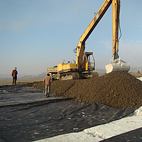 Escavatore al lavoro, stendendo il terreno sul tessuto di rinforzo Basetrac® Woven posato in opera