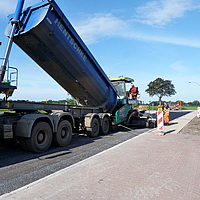 Un autocarro scarica l'asfalto in una macchina a termine per l'asfaltatura di una strada con il materiale composito SamiGrid®.