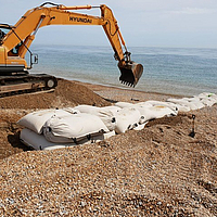 Installazione di SoilTain Bags su una spiaggia di ghiaia con un escavatore per la protezione dalle inondazioni