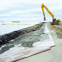 Una draga copre le stuoie di controllo dell'erosione installate con l'aiuto dei ripari in riva al mare.